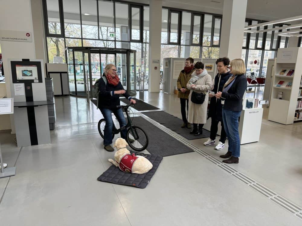 Im großzügigen Vorraum der Bibliothek sieht man Vertreter der Bibliothek und der Presse, Frau Dr. Denninger und das Assistenzhundteam.